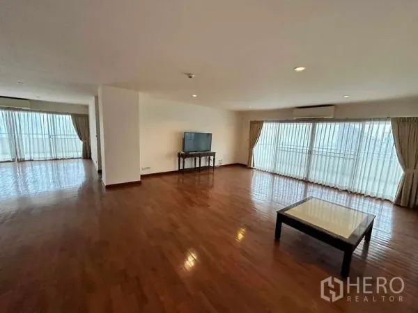 Condominium for rent in Bangkok - Expansive living room with parquet flooring, TV console and full-height windows opening to a balcony.