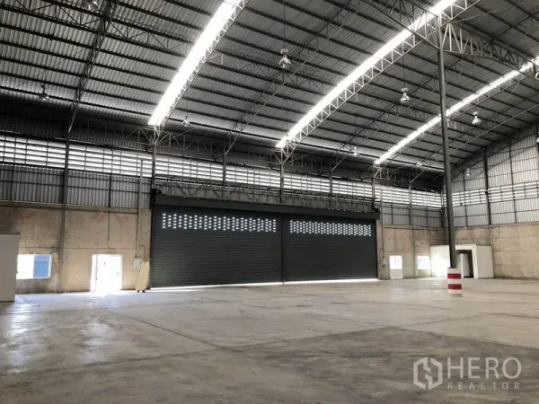 Warehouse for rent in Lam Luk Ka, Pathum Thani - Open-plan storage hall with triple roller shutters and bright strip lighting.