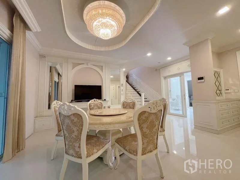 Detached House for rent or sale in Bang Phli, Samut Prakan - Bright dining area with round table, chandelier, TV wall, and staircase in the background.