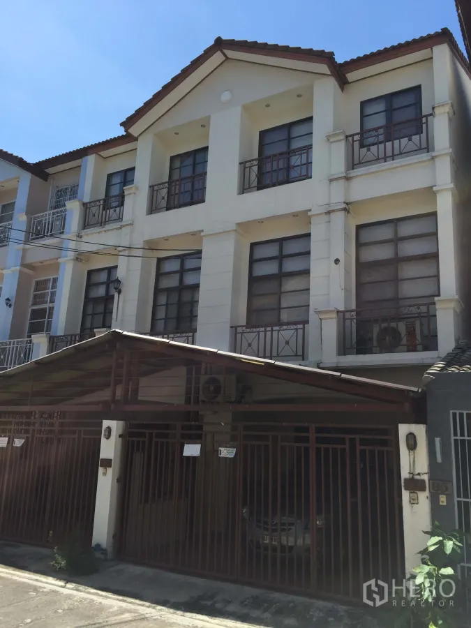 Townhouse for sale in Phra Khanong, Bangkok - Three-storey townhouse exterior in Phra Khanong with balconies, tiled roof and a gated covered carport on a quiet lane.
