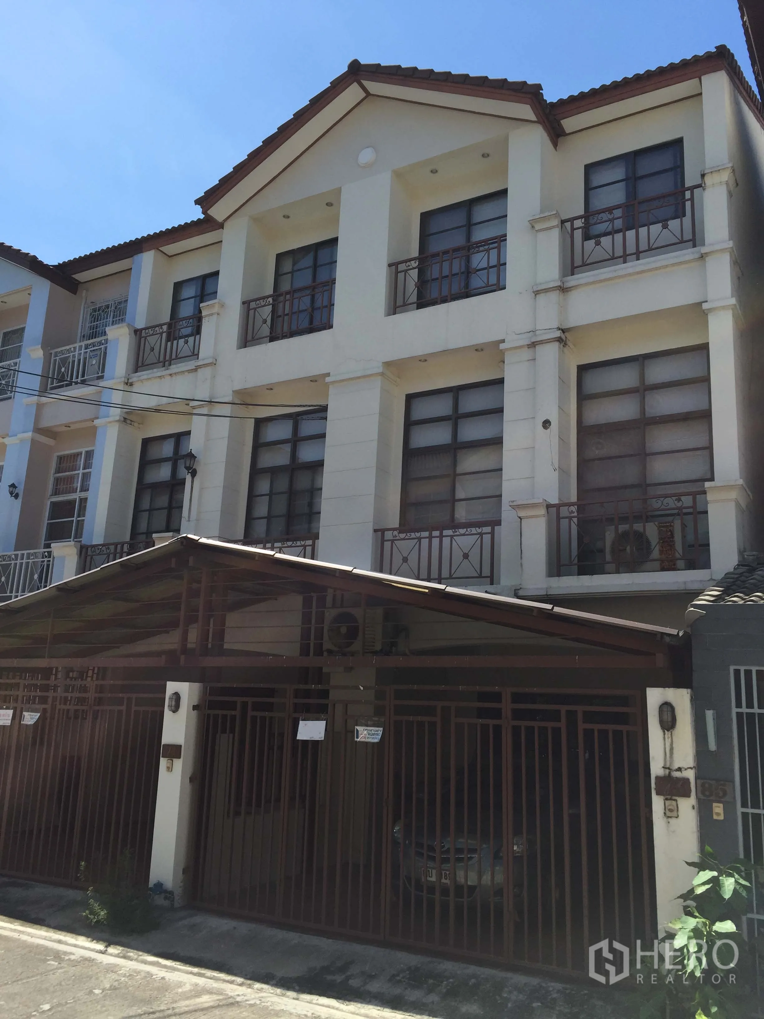 Townhouse for sale in Phra Khanong, Bangkok - Three-storey townhouse exterior in Phra Khanong with balconies, tiled roof and a gated covered carport on a quiet lane.