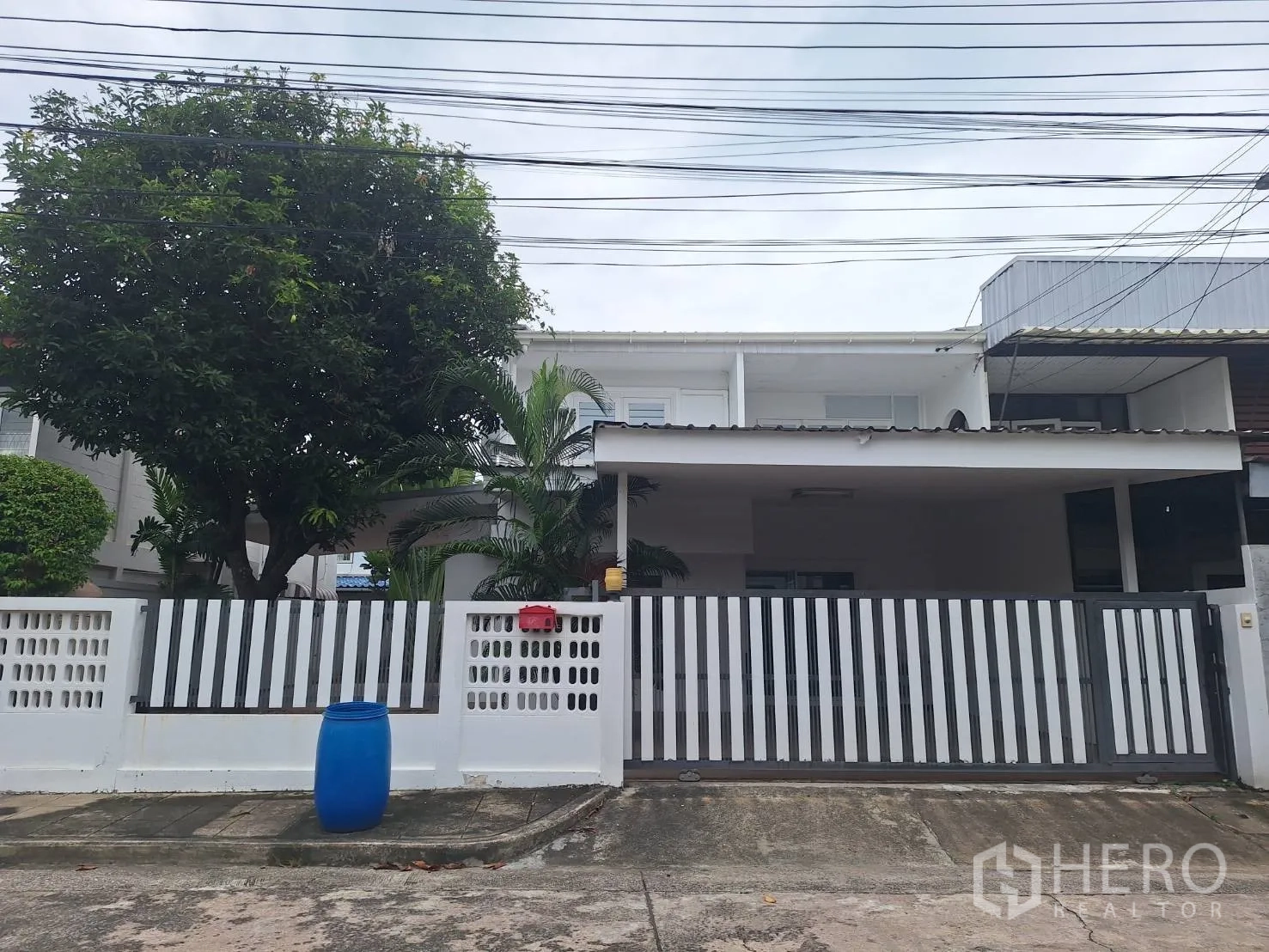 独栋房屋 for rent in Saphan Sung, Bangkok - 白色独立屋外观，条纹金属大门、带顶门廊与茂盛庭树。