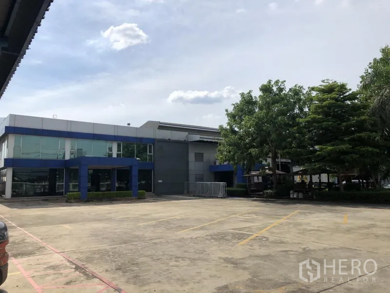 工厂 出租在Lam Luk Ka, Pathum Thani - 现代两层玻璃幕墙办公楼，邻接厂房与停车区。