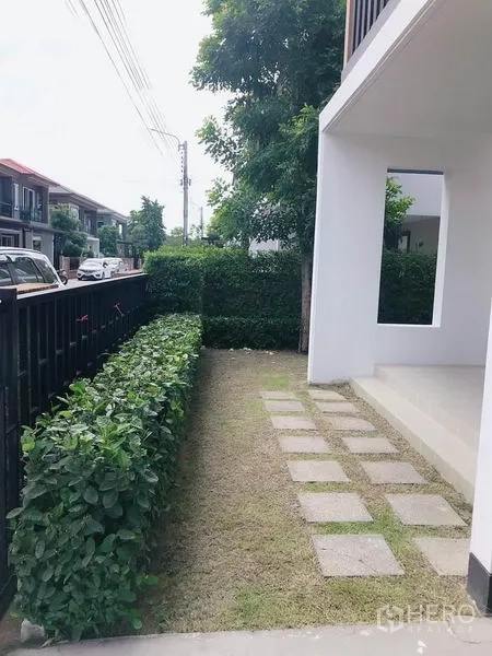 Detached House for sale in Suan Luang, Bangkok - Front garden path with stepping stones and low shrubs by the black fence.