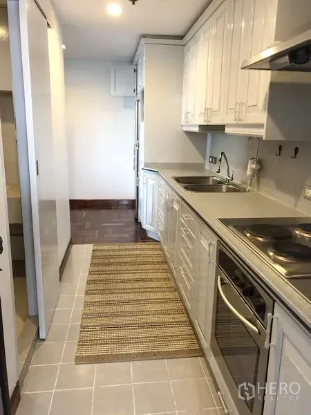 Condominium for rent or sale in Watthana, Bangkok - Fitted kitchen from another angle showing electric stove, hood and long countertop.