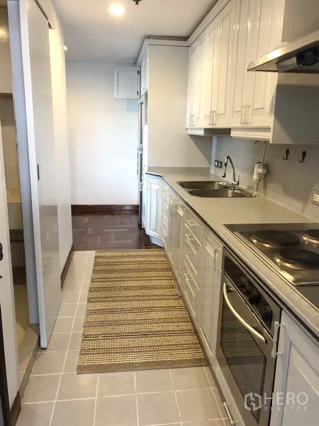 Condominium for rent or sale in Watthana, Bangkok - Fitted kitchen from another angle showing electric stove, hood and long countertop.