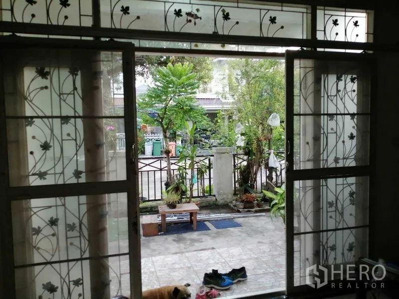 独立式住宅 出售在Prawet, Bangkok - 带花纹铁艺的推拉玻璃门，通向前院露台与花园。
