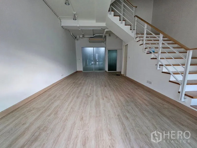 联排别墅 出租在Wang Thonglang, Bangkok - 开放式客厅，高挑天花与木地板，木质扶手楼梯通往二层。