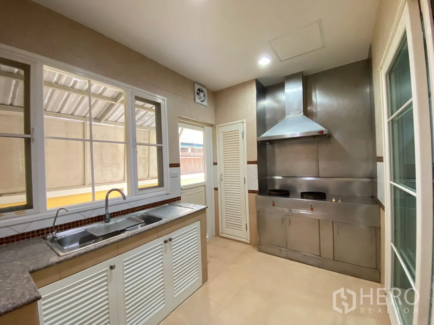 Detached House for rent in Phra Khanong, Bangkok - Enclosed kitchen with stainless cooktop and hood, double burners, sink, cabinets, and windows.