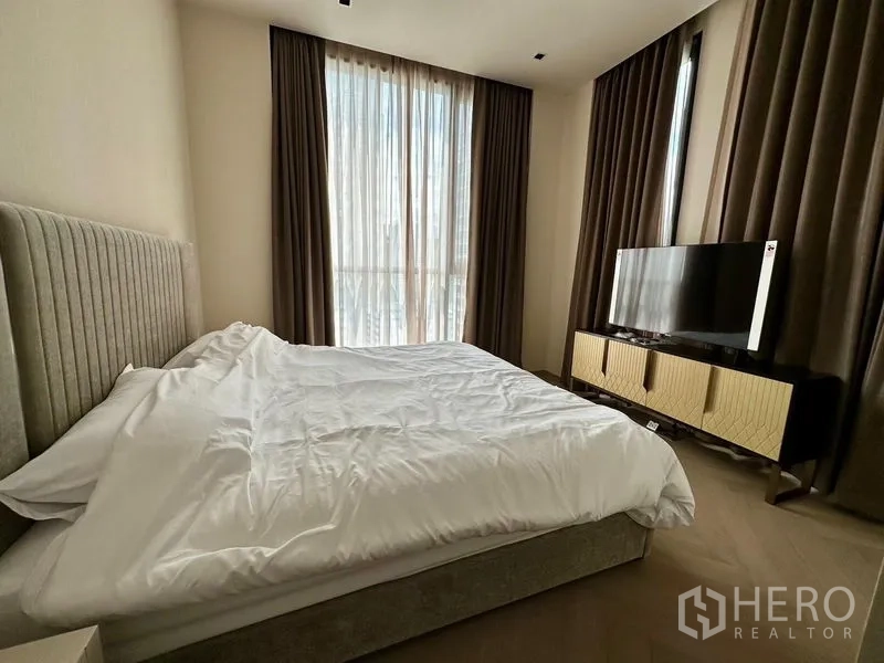 Condominium for rent - Bedroom with large corner windows, blackout curtains, and a TV cabinet opposite the bed.