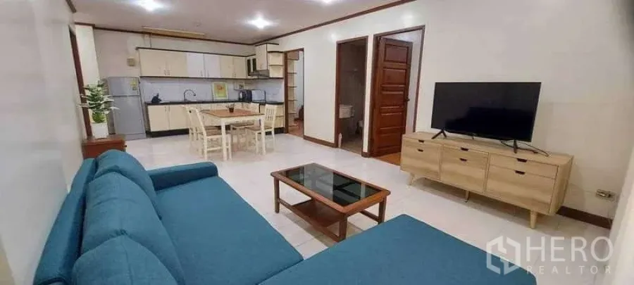 Condominium for rent in Khlong Toei, Bangkok - Another angle of the open living area showing blue sofa, TV console, dining table and adjoining kitchen.