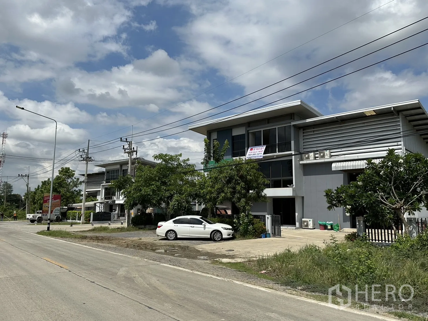 Factory for rent or sale in Pathum Thani - Streetscape of modern factory units along a wide road.