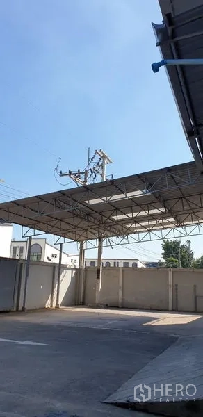 Warehouse for rent in Lam Luk Ka, Pathum Thani - Steel canopy structure over an open yard with utility lines against a blue sky.