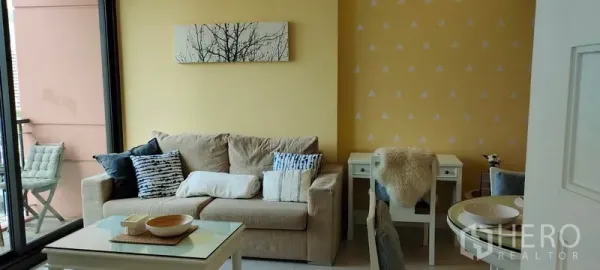 Condominium for rent or sale in Khlong Toei, Bangkok - Cozy living room with beige sofa, coffee table and balcony access in Aguston Sukhumvit 22.