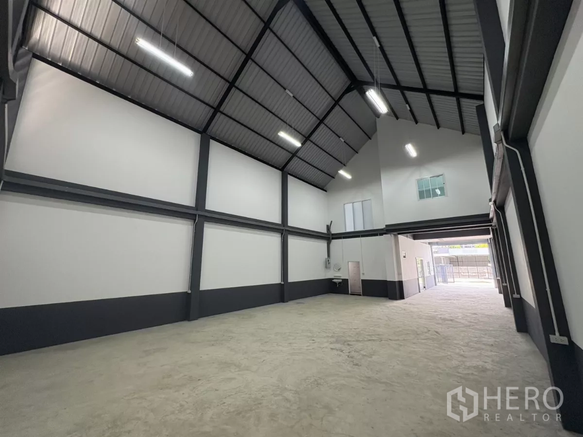 Factory for rent or sale in Bang Bua Thong, Nonthaburi - Long warehouse bay facing the entrance with exposed steel beams and LED lighting.