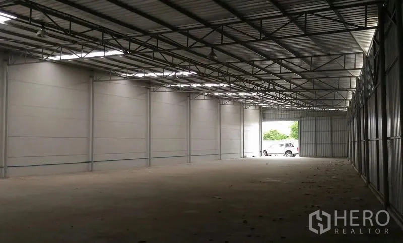 Warehouse for rent in Pathum Thani - Warehouse bay with high ceiling, steel beams, and vehicle access at the far end.