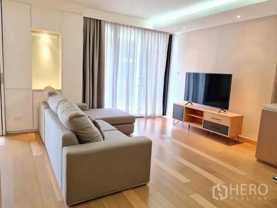 Condominium for rent in Watthana, Bangkok - Living area with sectional sofa, media unit and full-height curtains providing natural light.