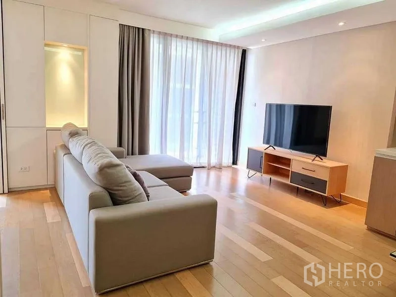 Condominium for rent in Watthana, Bangkok - Living area with sectional sofa, media unit and full-height curtains providing natural light.