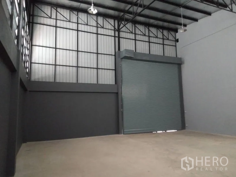 Factory for rent or sale in Lam Luk Ka, Pathum Thani - High-bay warehouse interior with large roller shutter door and steel roof.