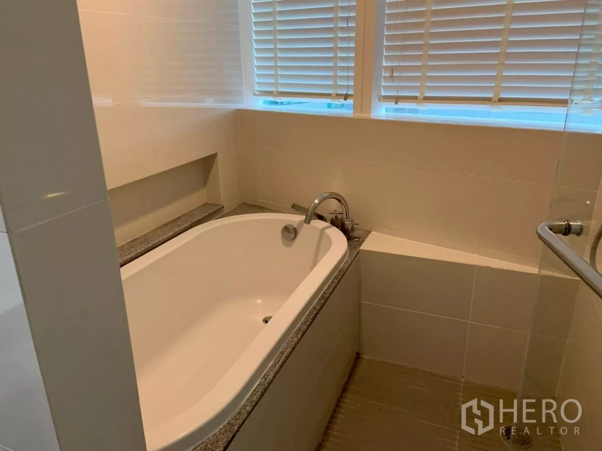 Condominium for rent in Khlong Toei, Bangkok - Bathtub with tiled surround and window blinds.