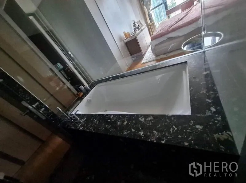 Condominium for rent in Khlong Toei, Bangkok - Luxury bathroom with deep soaking tub set in dark stone surround.