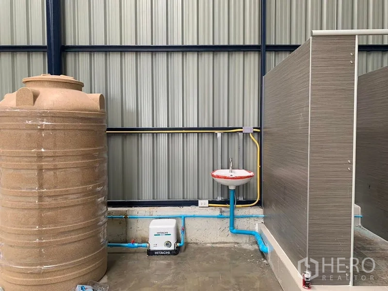 Warehouse for rent in Ban Pho, Chachoengsao - Utility area inside the warehouse with water tank, pump, sink, and restroom cubicle installed.