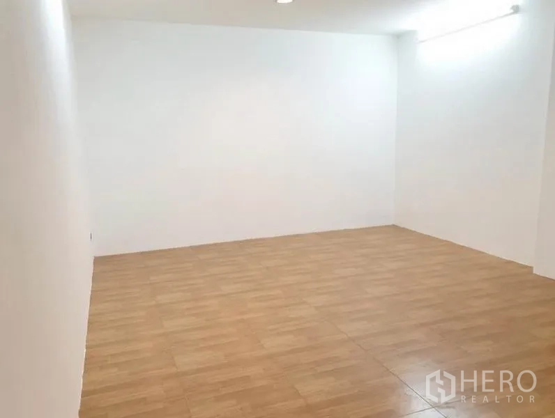 Townhouse for rent or sale in Chatuchak, Bangkok - Large empty room with wood laminate flooring and bright white walls.
