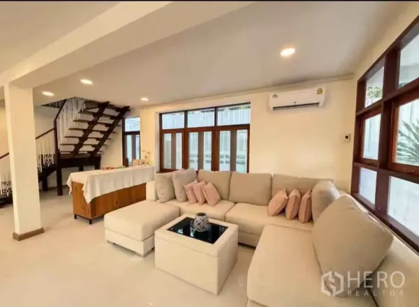独立式住宅 出租在Khlong Toei, Bangkok - 客厅另一角度，转角沙发、空调、长条窗与木楼梯。