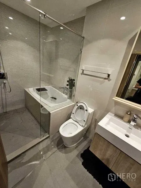 Condominium for rent - Bright bathroom with bathtub, glass shower screen, vanity and tile walls.