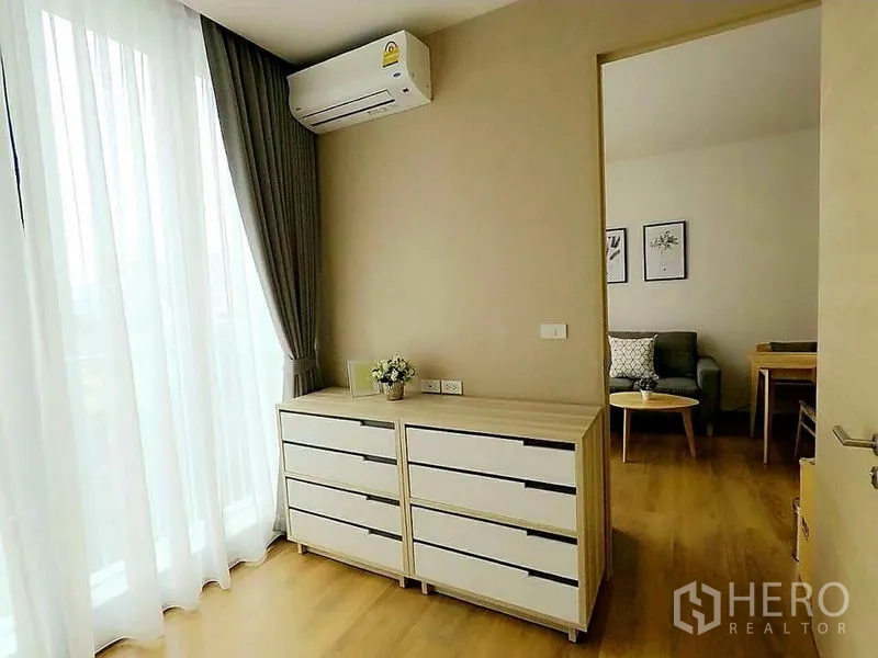 Condominium for rent in Khlong Toei, Bangkok - Corner with twin dressers, floor-to-ceiling sheer curtains and wall-mounted air conditioner.