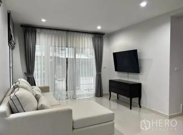 บ้าน ให้เช่าในSuan Luang, Bangkok - ห้องนั่งเล่นสว่าง โซฟาเข้ามุม ทีวีติดผนัง และประตูบานเลื่อนผ้าม่านโปร่ง