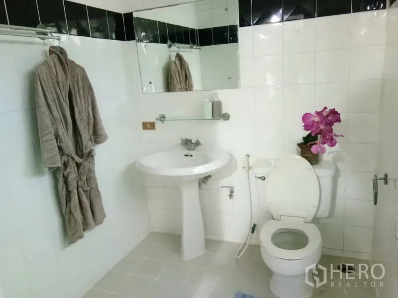 Condominium for rent in Watthana, Bangkok - White-tiled bathroom with pedestal sink, toilet and wall mirror.