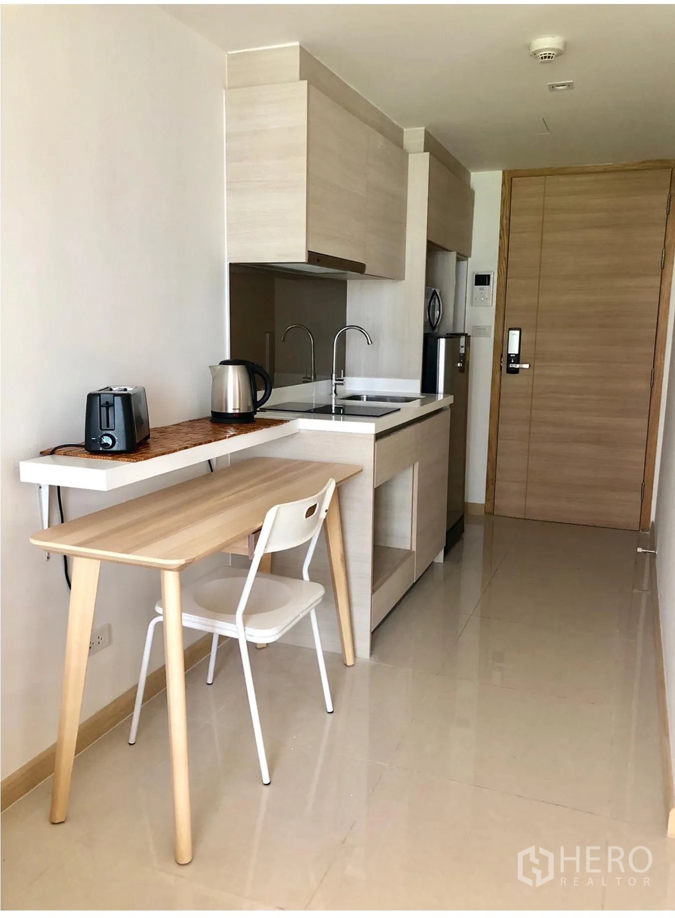 Condominium for rent in Watthana, Bangkok - Compact kitchenette with light wood cabinets, sink and a small breakfast table.