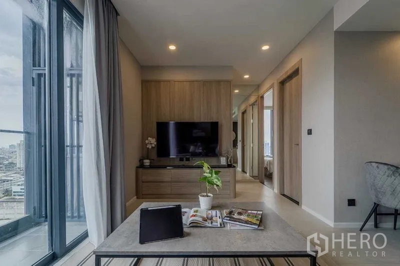 Condominium for rent in Pathum Wan, Bangkok - Living room with TV cabinet, sliding doors and open city view beyond the balcony.