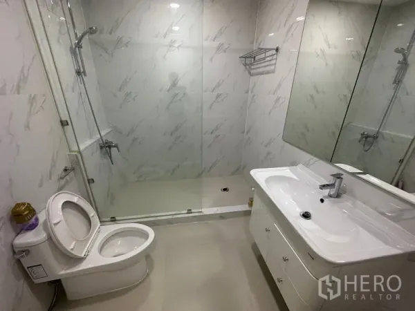 Condominium for rent in Watthana, Bangkok - Modern bathroom with glass shower enclosure, marble-look tiles, vanity and toilet.