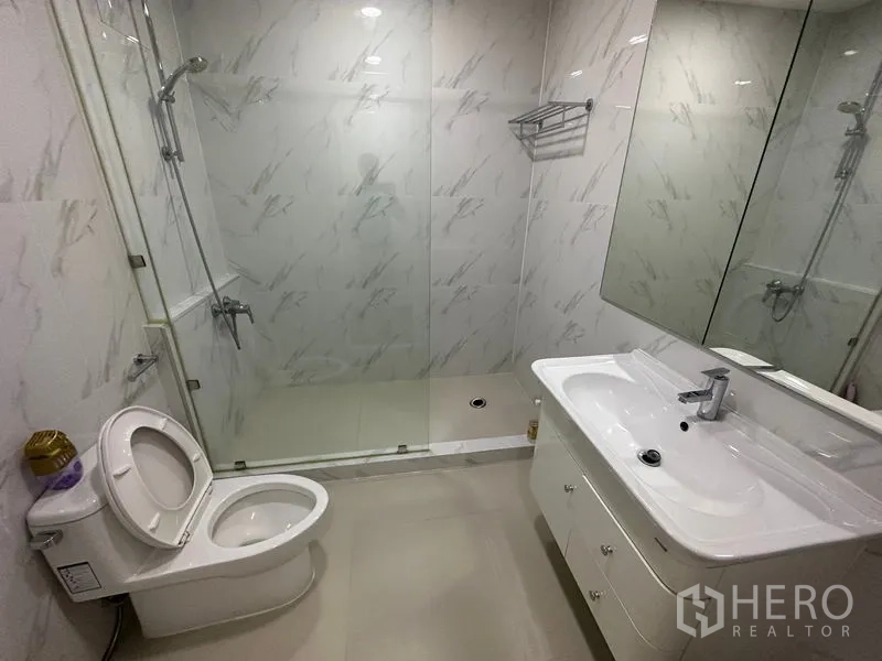 Condominium for rent in Watthana, Bangkok - Modern bathroom with glass shower enclosure, marble-look tiles, vanity and toilet.