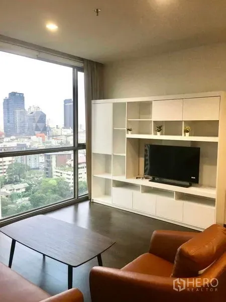 Condominium for rent - Cozy lounge with large window and Bangkok skyline view, white shelving and brown sofa.