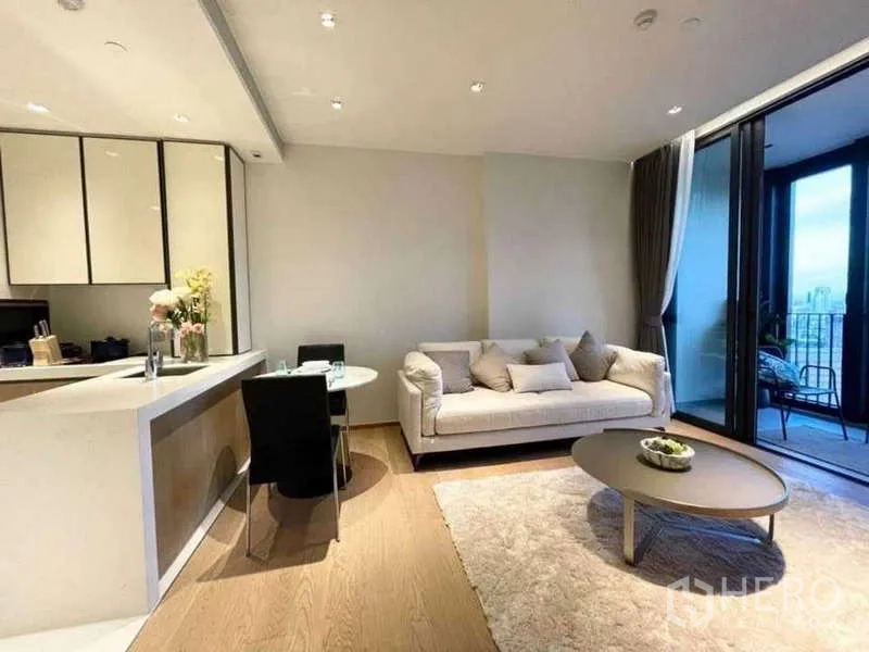Condominium for rent or sale in Khlong Toei, Bangkok - Living room with sofa, dining nook, and sliding doors opening to a balcony.