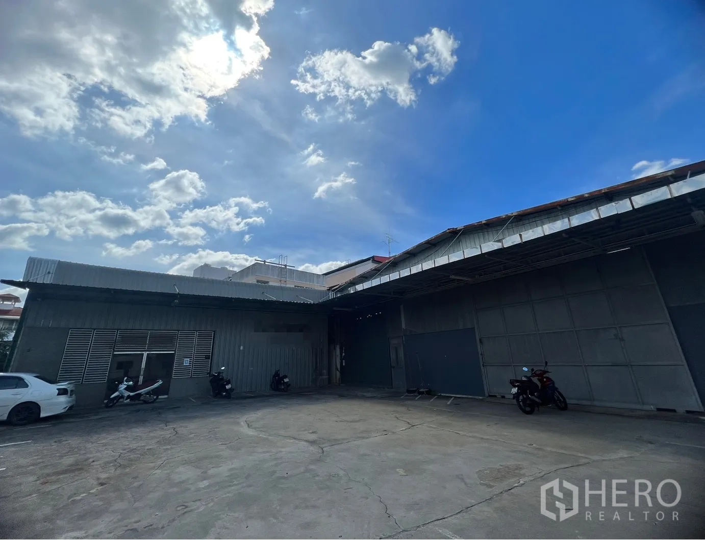货栈 出租在Suan Luang, Bangkok - 曼谷金属板仓库外立面，宽阔混凝土装卸场与停车区，天空晴朗。