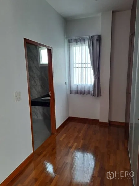 独立式住宅 出租在Prawet, Bangkok - 卧室一角，带套间门、窗户与窗帘，木地板。