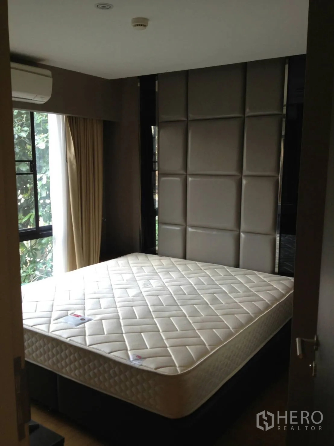 Condominium for rent in Khlong Toei, Bangkok - Cozy bedroom with padded headboard, large window and mattress.