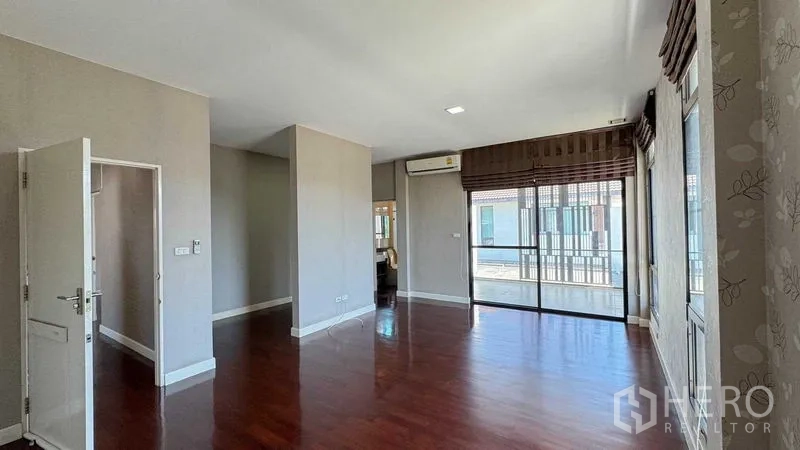Detached House for sale in Bang Kapi, Bangkok - Spacious upstairs bedroom with wood floors, sliding doors to the balcony, and abundant natural light.