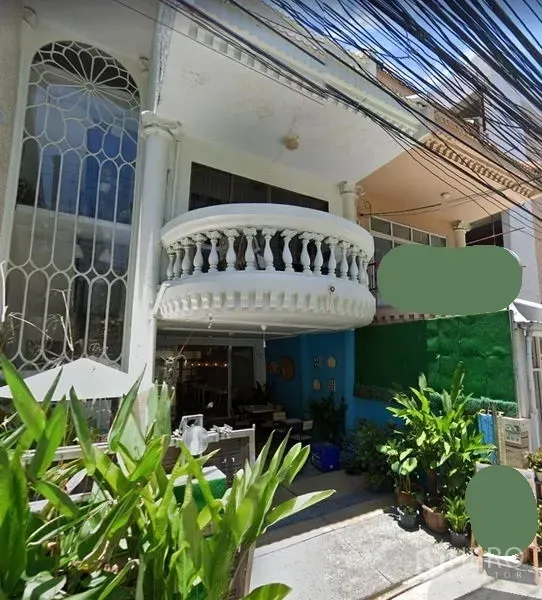 联排别墅 出租在Watthana, Bangkok - 曼谷联排别墅外观，白色立面带圆形阳台与拱形窗，入口有绿植与前庭，白天街景可见电缆。