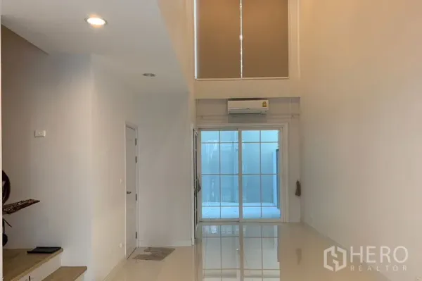 联排别墅 出租在Bang Na, Bangkok - 挑高客厅，亮面地砖、空调与高窗，连接落地推拉门
