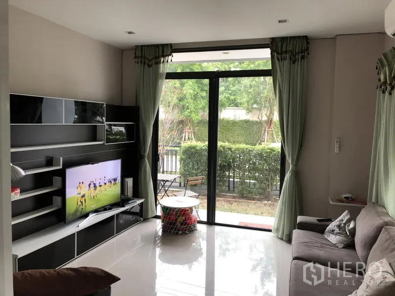 Detached House for rent in Saphan Sung, Bangkok - Bright living room with TV wall unit, sofa and sliding glass doors opening to the garden.