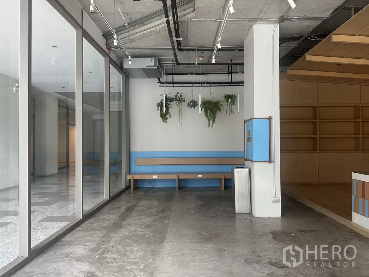 Retail Space for rent - Corner near the glass wall with a long bench and decorative plants beside wooden shelving.