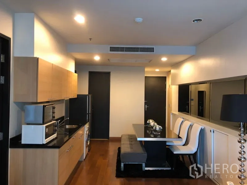 公寓 出租在Pathum Wan, Bangkok - 开放式厨房与餐区，浅色木柜、黑色台面与长椅，帕吞旺公寓内部。