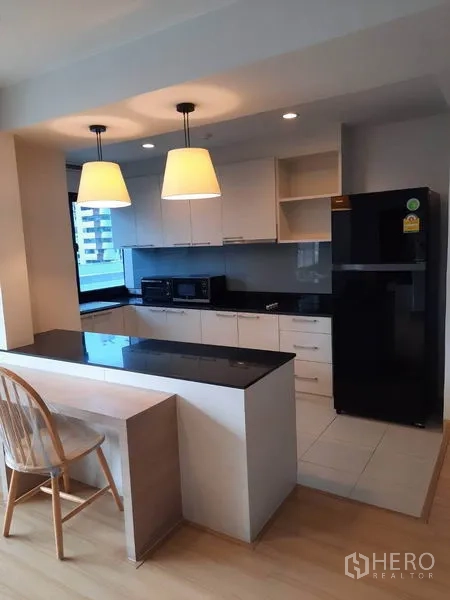 Condominium for rent in Watthana, Bangkok - Modern white kitchen with black stone countertop, breakfast bar and pendant lights, overlooking city views.