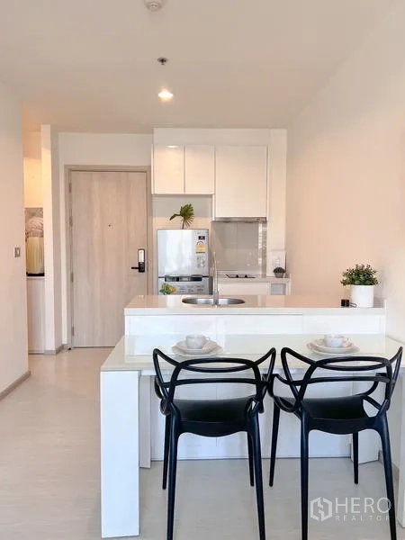 Condominium for rent or sale in Khlong Toei, Bangkok - White kitchen with breakfast bar, two black chairs and built-in cabinetry.