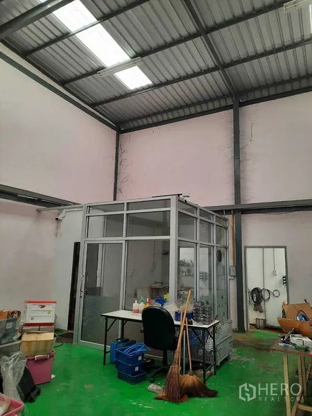 Warehouse for sale in Samut Prakan - Small glass office room beneath a high ceiling with tools and storage nearby.
